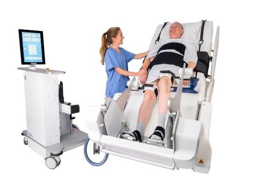 Pflegekraft betreut älteren Mann auf Reha-Trainingsgerät mit Monitor
