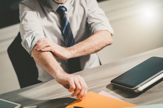 Mann im Hemd krempelt Ärmel am Schreibtisch mit Laptop, Tablet und Papier hoch