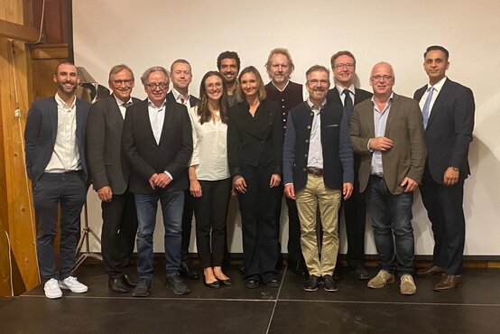 Gruppenfoto von 12 Personen – Männer und Frauen in formeller und business-casual Kleidung – bei Klinikveranstaltung vor weißer Wand