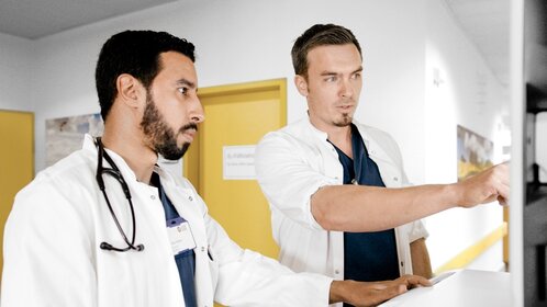 Zwei Assistenzärzte im Klinikflur besprechen Daten am Computer