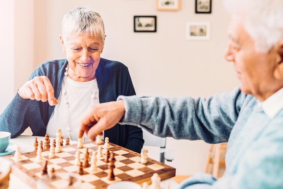 Zwei ältere Personen mit grauen Haaren spielen Schach an einem Tisch