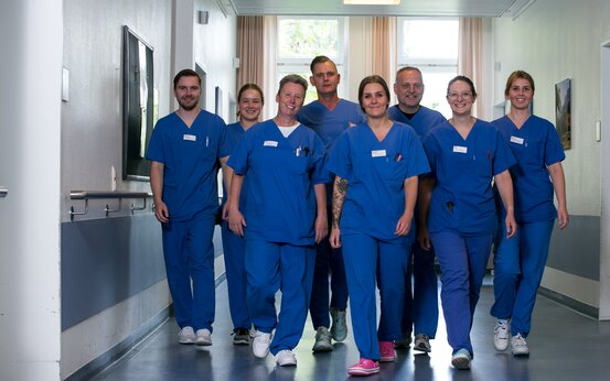 Achtköpfiges Team in blauer medizinischer Kleidung geht lächelnd durch hellen Krankenhausflur