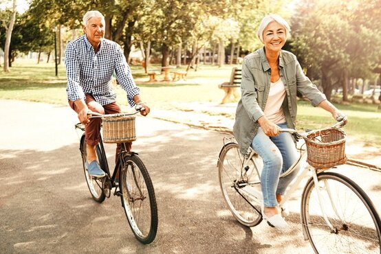 Älteres Paar fährt lächelnd Fahrrad auf sonnigem Parkweg