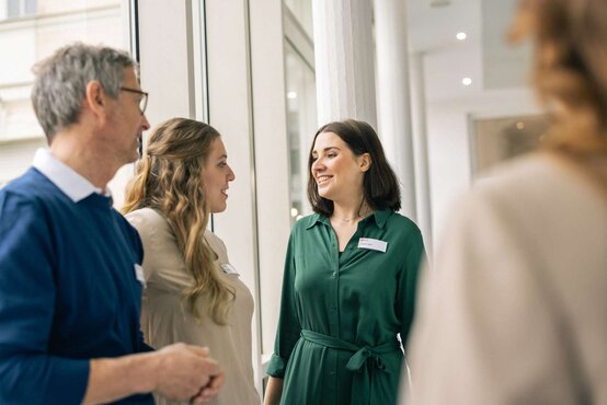 Drei Personen mit Namensschildern unterhalten sich freundlich im hellen Flur