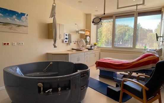 Heller Kreißsaal der Schön Klinik Rendsburg mit großer, runder Badewanne, verstellbarem Bett mit roten und weißen Tüchern