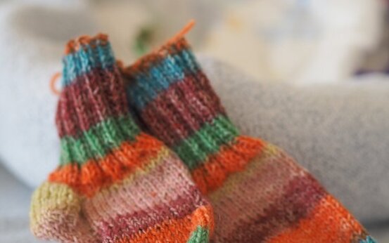 Zwei gestrickte, bunte Wollsocken liegen nebeneinander auf einer Decke