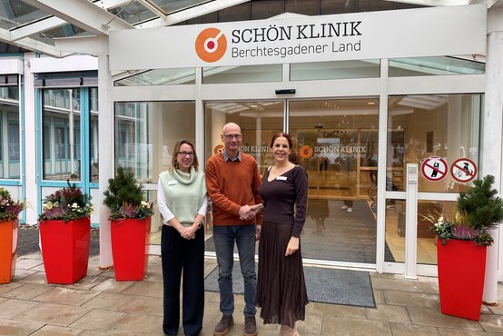 Drei Personen mit Namensschildern vor dem Eingang der Schön Klinik Berchtesgadener Land