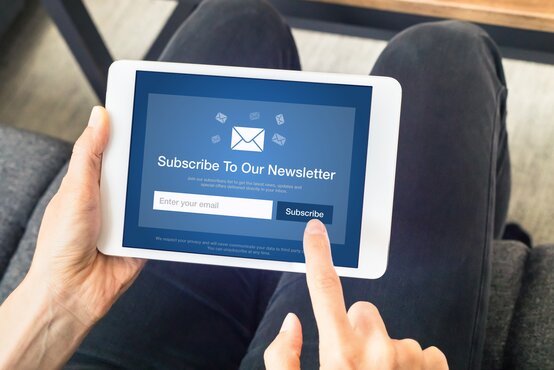 Person hält Tablet mit Newsletter-Anmeldeformular, Finger tippt auf „Subscribe“-Button