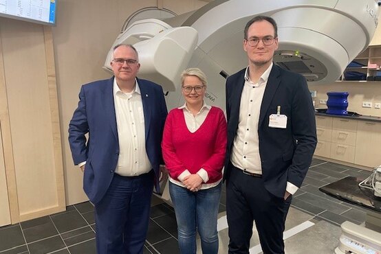 Drei Personen vor Linearbeschleuniger im modernen Behandlungsraum der Schön Klinik Rendsburg