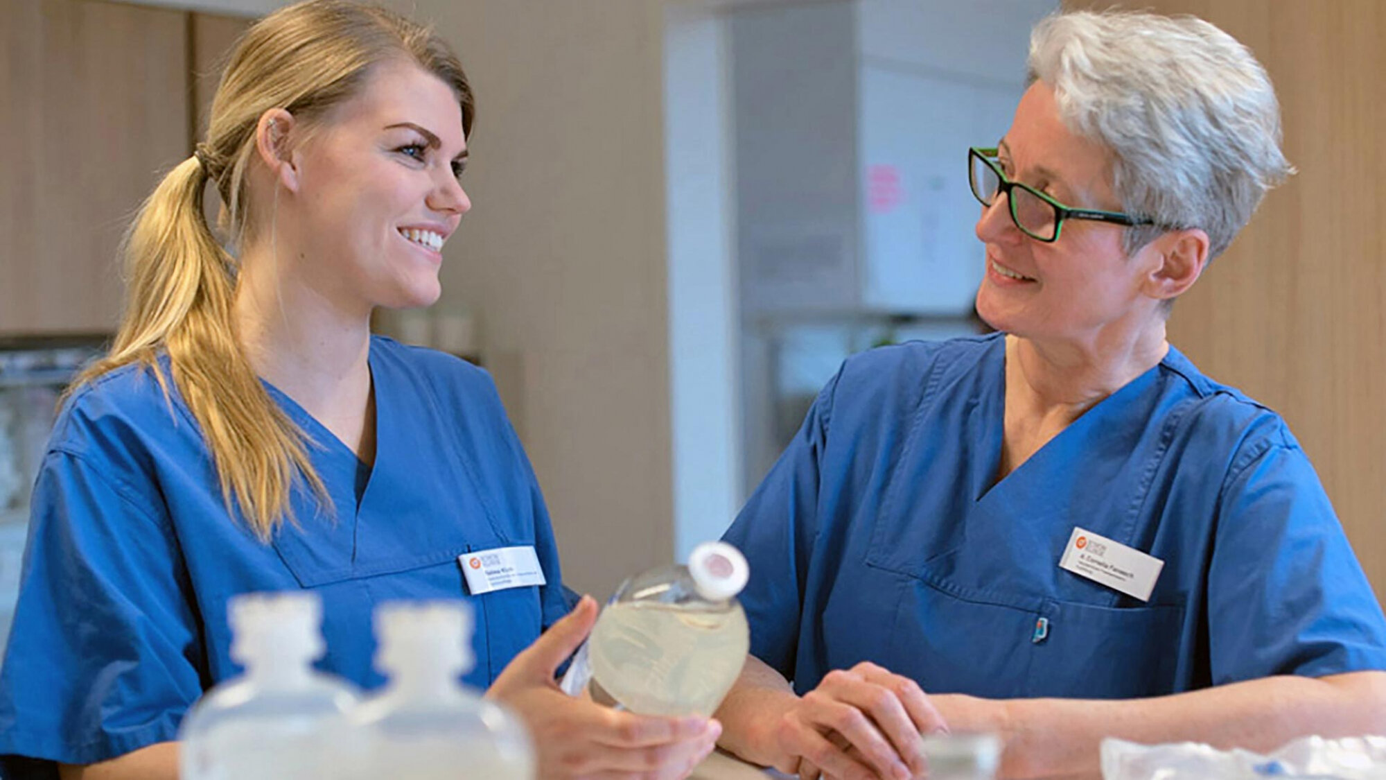 Junge und erfahrene Pflegekraft in blauer Kleidung bei Infusionsvorbereitung im Krankenhaus