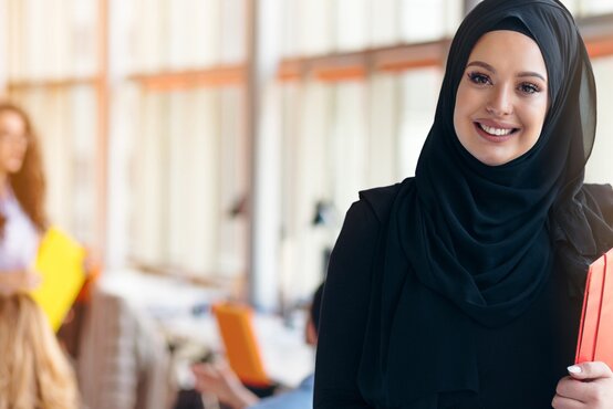 Junge Frau mit schwarzem Hijab hält roten Ordner und lächelt